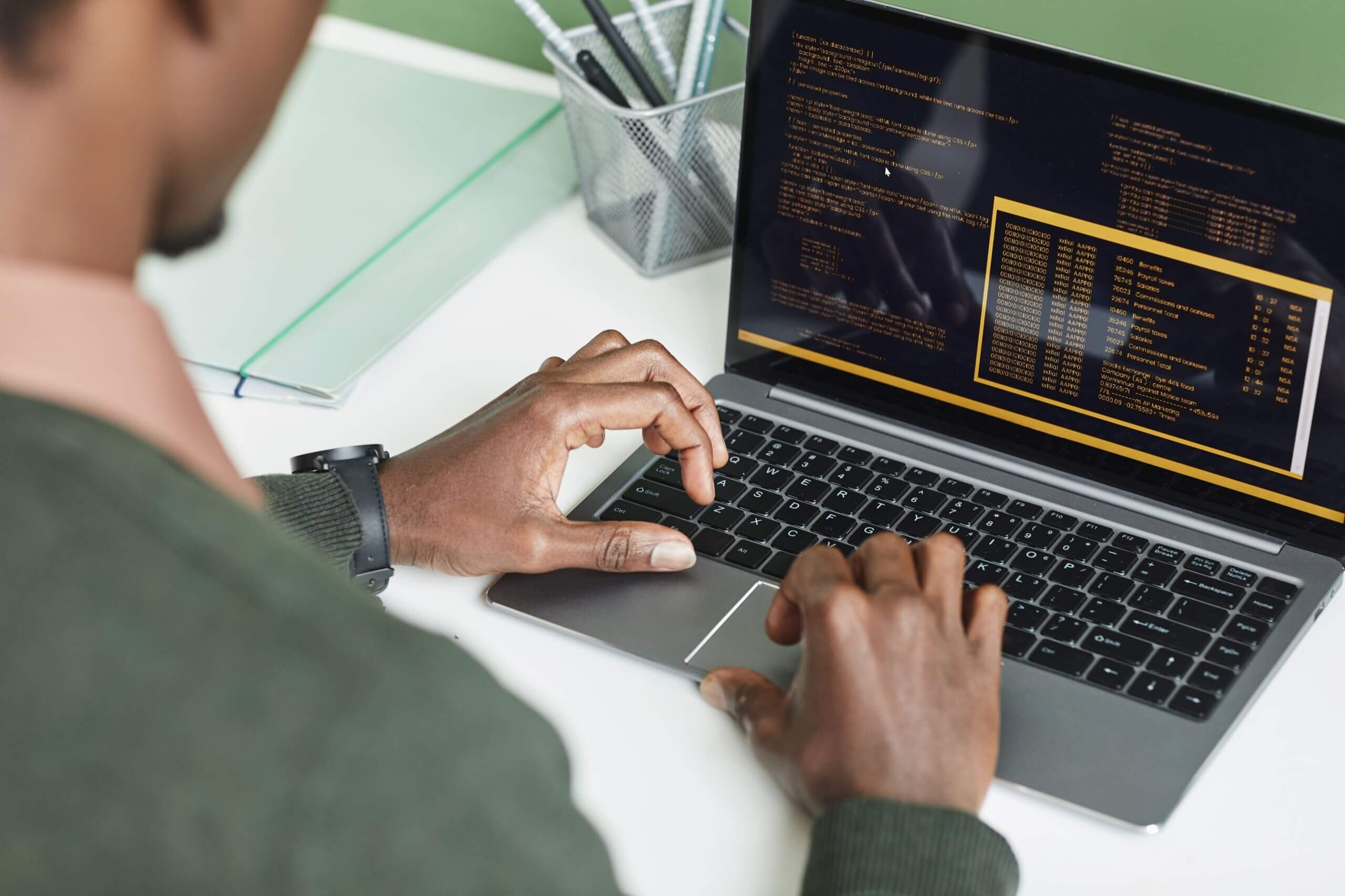 Pessoa preta trabalhando em um notebook em que é possível ver um trecho código. Capa do artigo "Fases de testes e Tipos de testes".