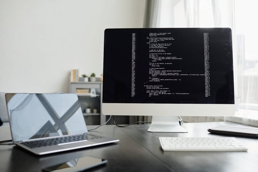Capa do artigo Desenvolvimento iOS com um computador desktop da Mac e códigos de programação nele.