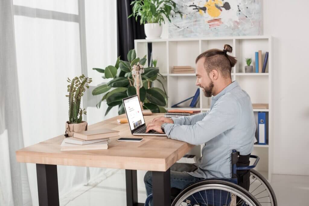 Capa do artigo "termo PCD e inclusão no mercado de trabalho" com um homem branco de perfil em uma cadeira de rodas enquanto usa um notebook.