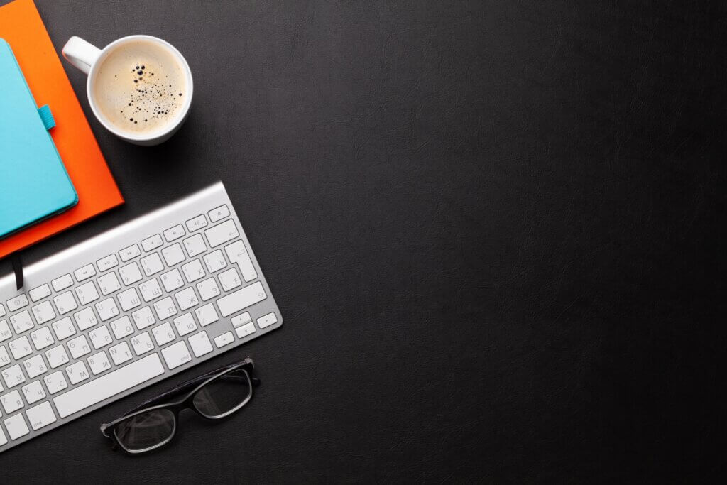 Capa do artigo Definition of Ready (DoR) em que vemos um fundo preto e no canto esquerdo um teclado de mac, uma xícara de café e alguns moleskines empilhados.