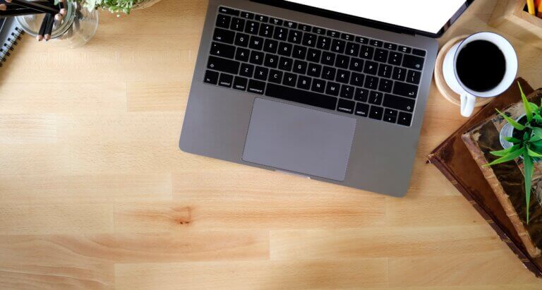 Capa do artigo sobre a ferramenta kind, usada para criar clusters locais no kubernetes. Na imagem se vê o teclado de um notebook em uma mesa de madeira e uma xícara de café ao lado.