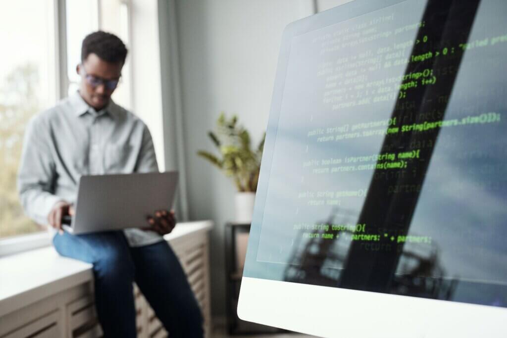 Capa do artigo Jakarta Data em que vemos um jovem negro usando laptop enquanto está sentado perto da janela no escritório de desenvolvimento de software ao fundo, enquanto vemos uma tela de código em primeiro plano.