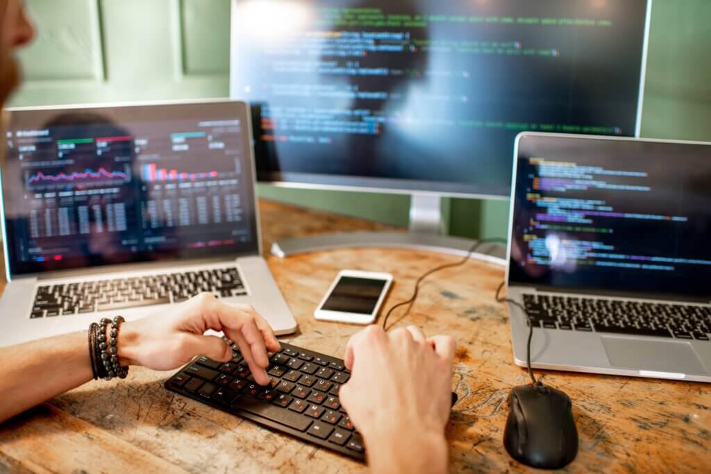 Capa do artigo sobre Engenharia de Software Empírica onde temos um jovem programador escrevendo um código de programa sentado no local de trabalho com três monitores.