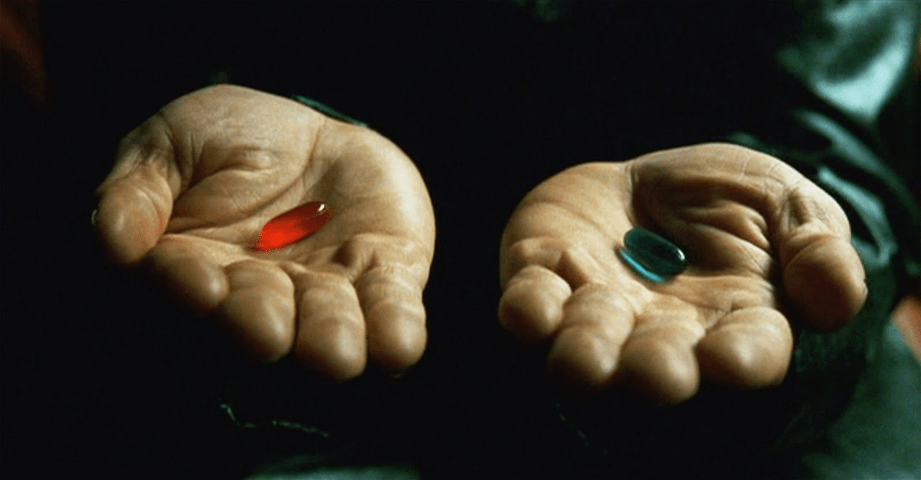 Foto de uma clássica cena do filme The Matrix (1999), em que o personagem Morpheus oferece duas pílulas para o protagonista. Na foto, com um fundo bastante escuro, temos uma pessoa, porém o foco da imagem não nos permite ver o resto do corpo, somente suas mãos. A pessoa, que é negra, está com suas duas mãos estendidas oferecendo pílulas: na mão direita, temos uma pílula de cor vermelha, e na direita uma pílula de cor azul, sugerindo que existe o poder de escolha entre os dois tipos de pílulas. 