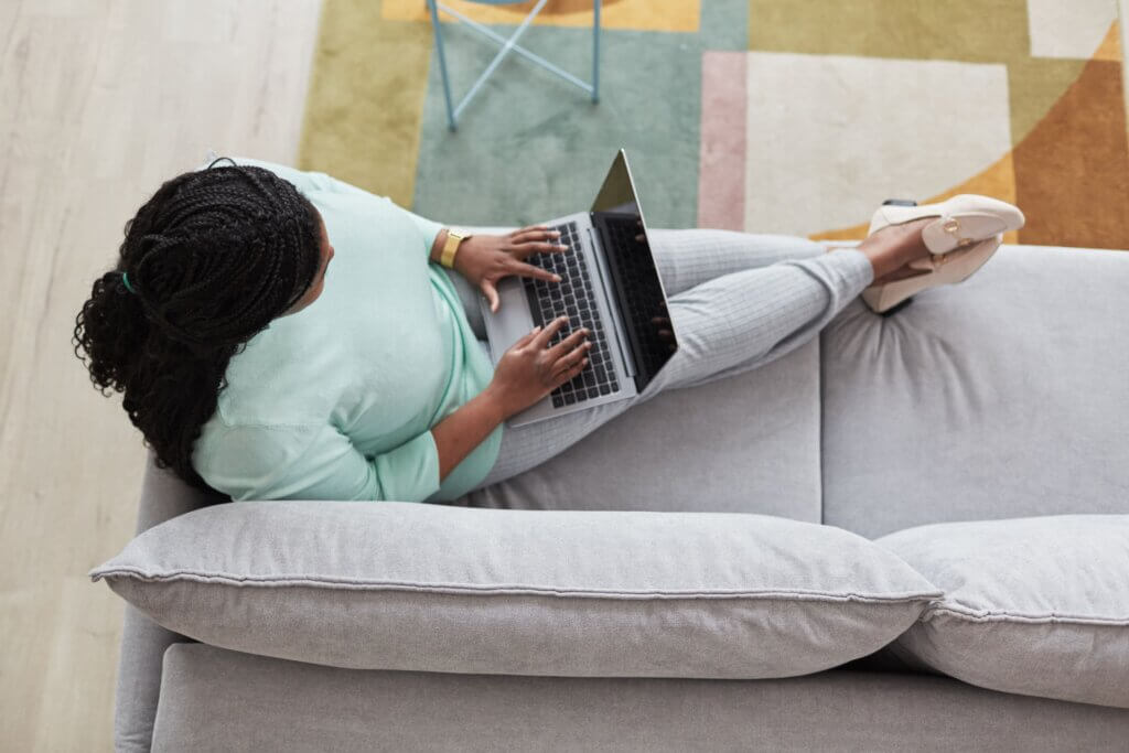 Capa do artigo sobre carreira em produtos. Na imagem, uma mulher negra de cabelos trançados está sentada em um sofá com o notebook no colo.
