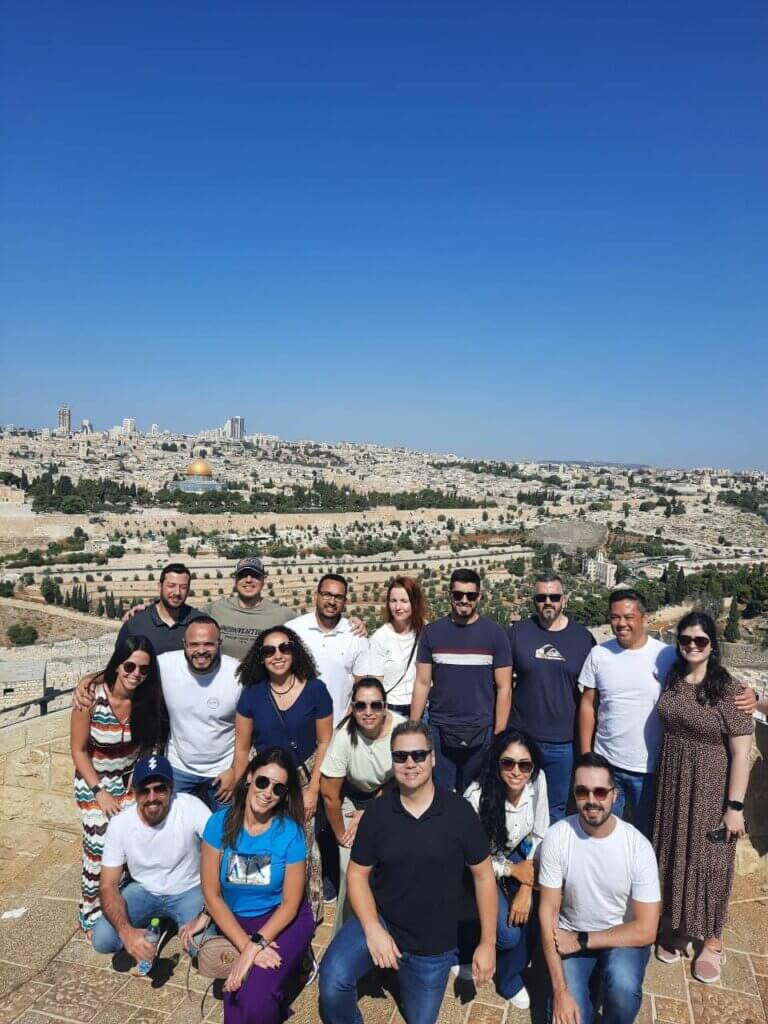Grupo de pessoas executivas em frente a cidade de Jerusalém. Ao fundo é possível ver, por exemplo, a Cúpula da Rocha ou Domo da Rocha, uma das construções mais características da cidade velha de Jerusalém.