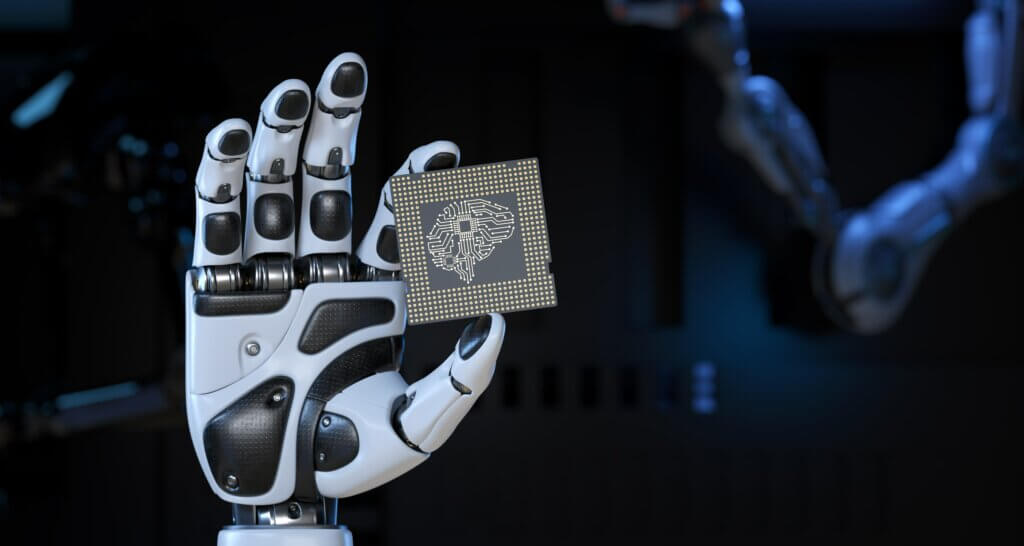 Imagem referente ao conteúdo "Aplicativos de Inteligência Artificial que usam suas fotos: o perigo por trás da moda", onde uma mão de um robô segura com a ponta dos dedos um chip com um cérebro desenhado.