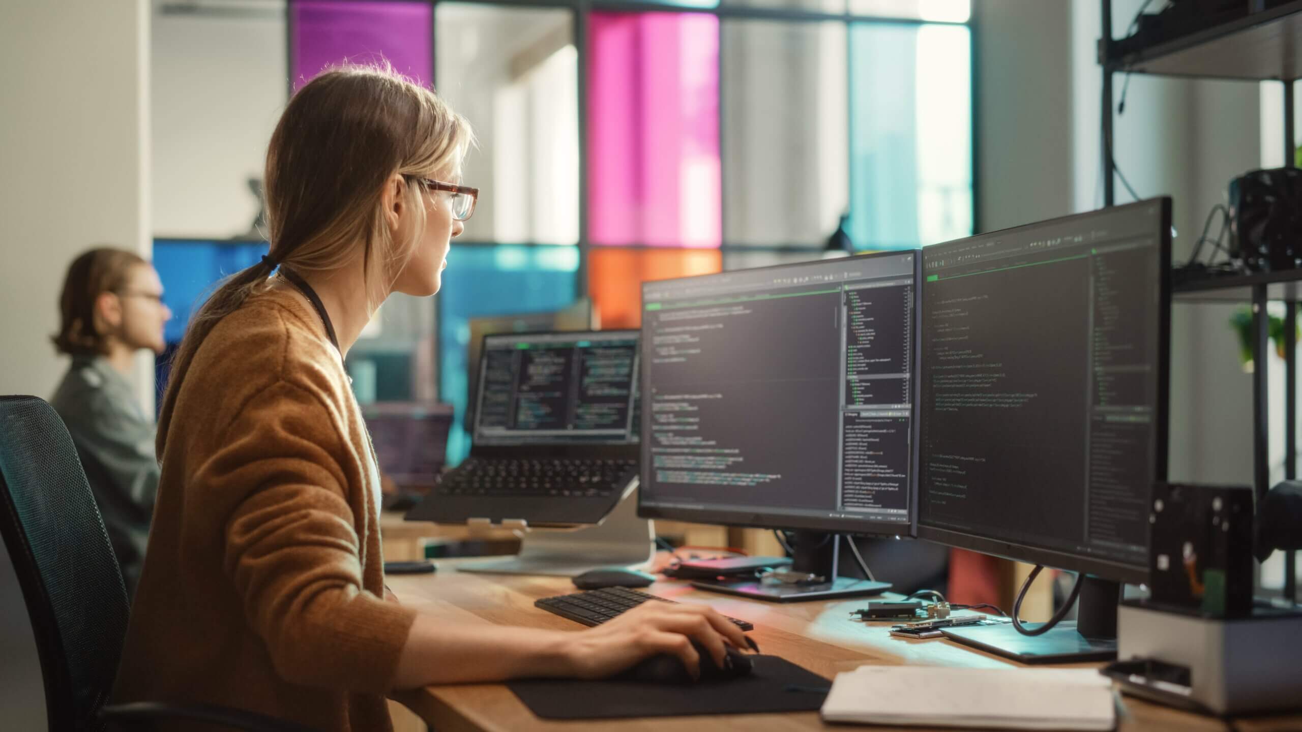 Imagem capa do conteúdo "Débito técnico", onde podemos ver Engenheira de software feminina escrevendo código no computador desktop com configuração de várias telas no elegante espaço de escritório de coworking.