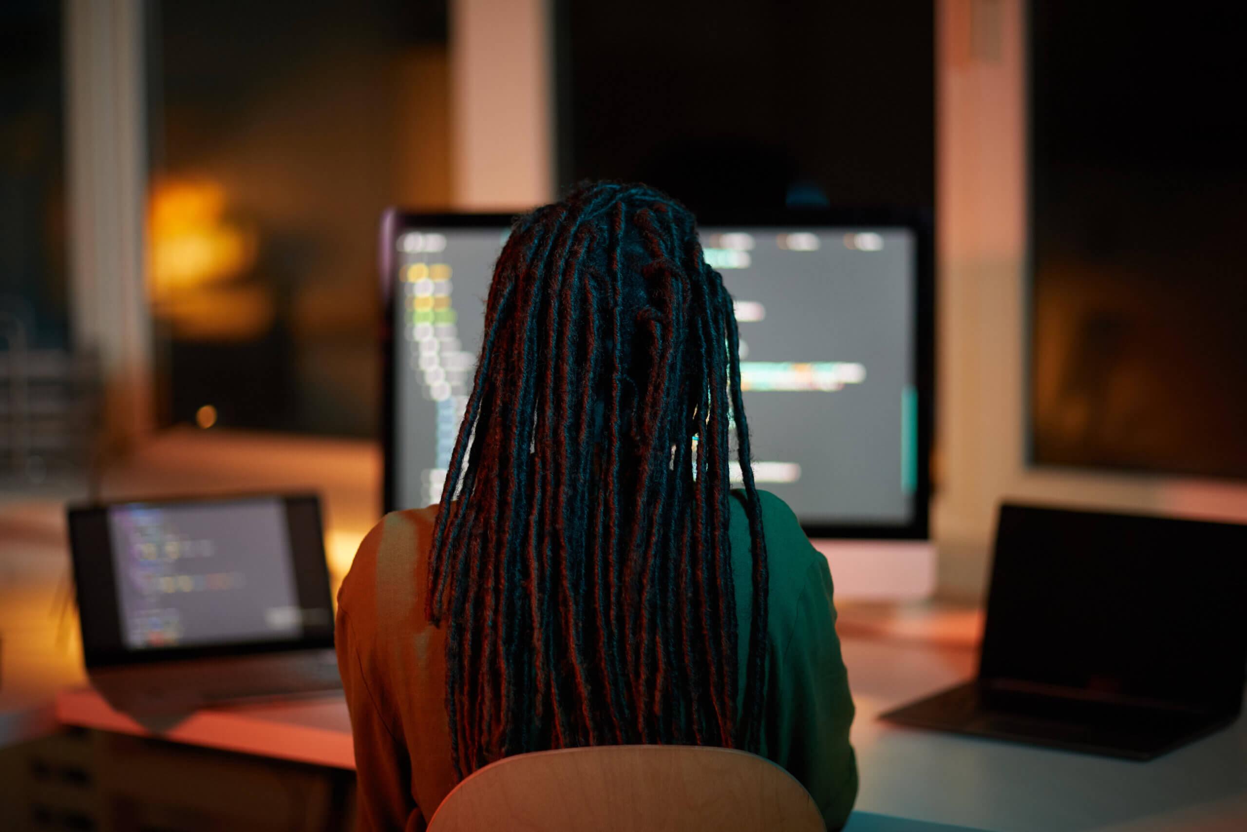Capa com a foto de uma mulher de cabelos trançados de costas de frente para um computador com códigos.